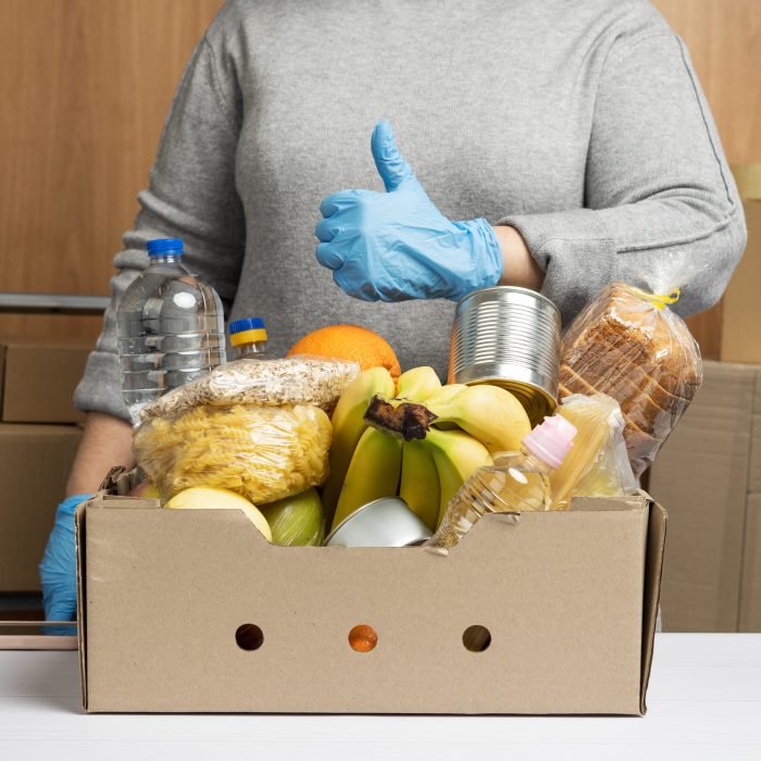 woman in gloves keeps collecting food, fruits and things and a cardboard box for helping those in need, the concept of help and volunteering. Delivery of products